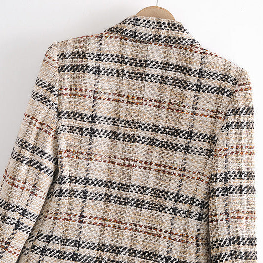 A close-up of a tweed blazer jacket hanging on a wooden hanger, featuring a textured plaid pattern in beige, black, and brown.