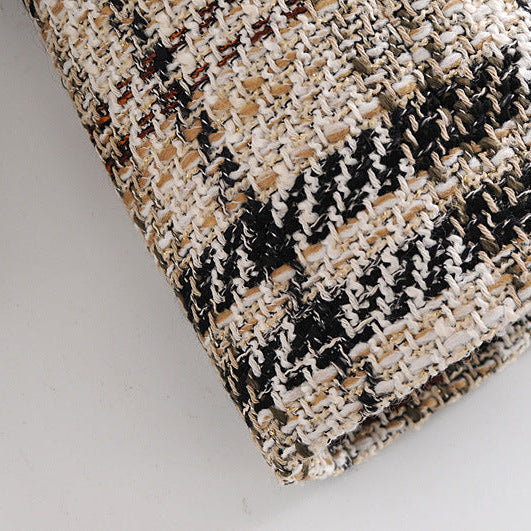 A close-up of a woven tweed fabric with a black, beige, and off-white pattern, showing the detailed texture of the material.