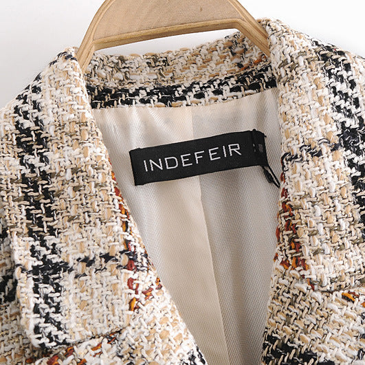 A close-up of a tweed blazer jacket by INDEFEIR, featuring a black, beige, and white textured weave with subtle orange and brown flecks, shown on a wooden hanger.