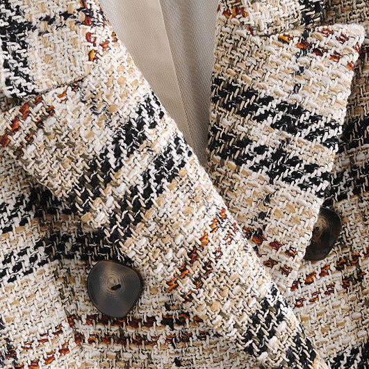 Close-up of a tweed blazer fabric with a black, beige, and white houndstooth-like weave, featuring dark buttons and a light inner lining.