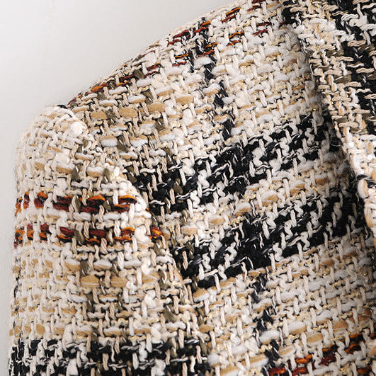 Close-up of a textured tweed fabric with a black, cream, and beige pattern, showing the woven material details.