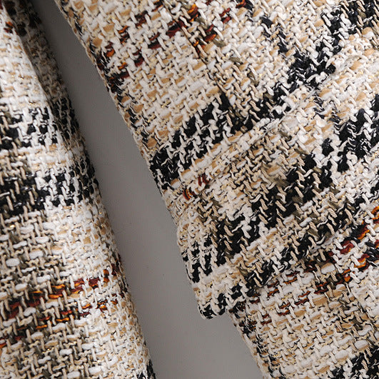 Close-up of a textured tweed fabric with a black, beige, and white houndstooth-like pattern, showing the weave detail and draped folds.