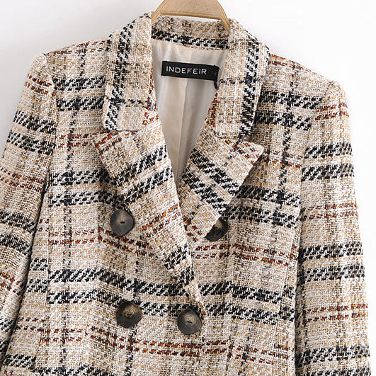 A close-up of a double-breasted tweed blazer on a wooden hanger, featuring a beige, black, and brown plaid pattern with dark brown buttons. The brand label 'INDEFEIR' is visible inside the collar.